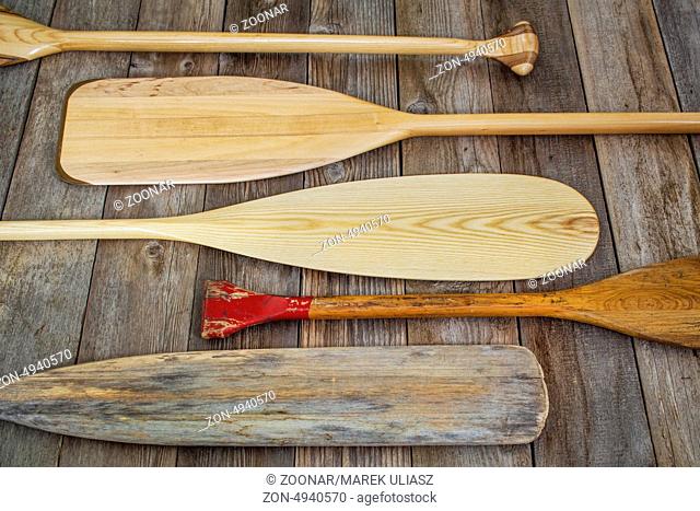 old and new wooden canoe paddles on a wood deck