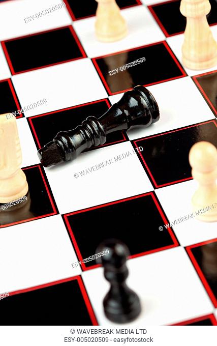 Black queen lying at the chessboard while white chessmen standing