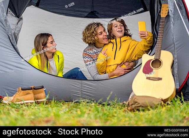 Three siblings taking smart phone selfie inside tent