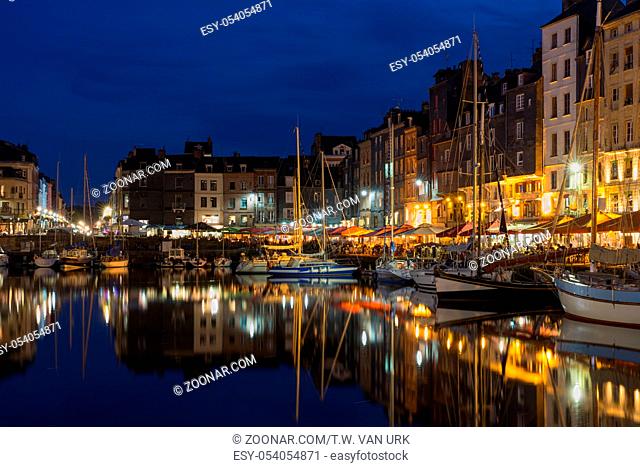 Illuminated harbor of Honfleur at night with many ships and restaurants, France