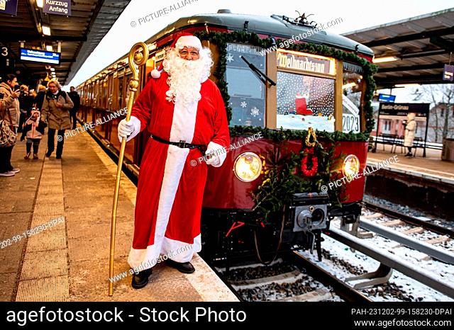 02 December 2023, Berlin: A man in a Santa Claus costume stands in front of the Historische S-Bahn association's Christmas train at Grünau S-Bahn station