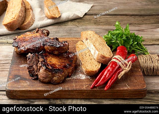 grilled pork steaks on the bone on a kitchen cutting board, baked sliced rye flour bread, top view