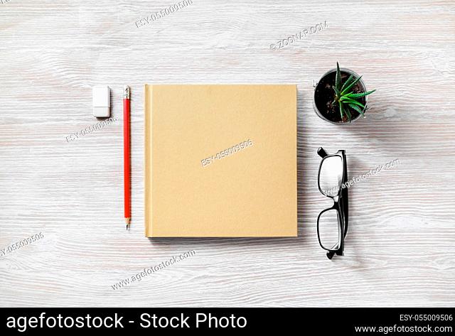 Closed book and blank stationery: glasses, pencil, eraser and plant on light wood table background. Top view. Flat lay