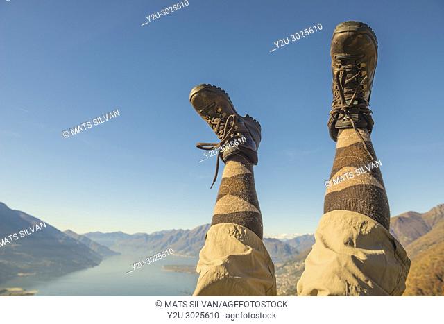 Hiking Shoes and Legs Up in the Air Over Alpine Mountain Range and Lake maggiore in Ticino, Switzerland