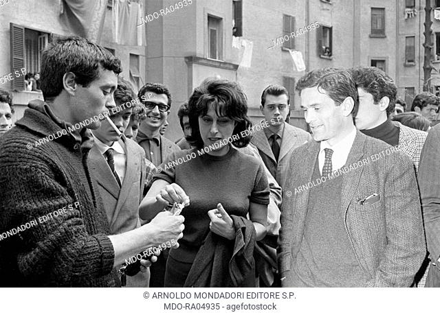 Italian actor Franco Citti giving a cigarette to Italian actress Anna Magnani in front of Italian director and writer Pier Paolo Pasolini and Italian actor...