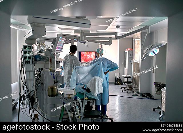 Operating room with equipment. Doctors are looking at the laparoscopy display while standing next to the patient on the surgical table. Horizontal