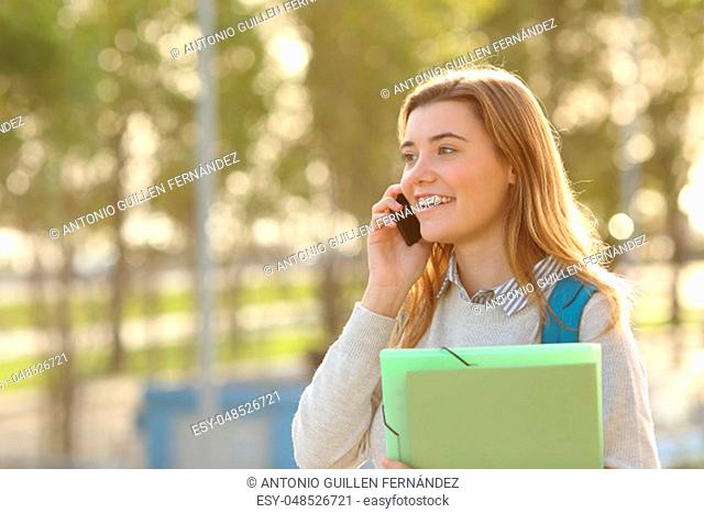Happy student girl walking and calling on mobile phone outdoors with a green background