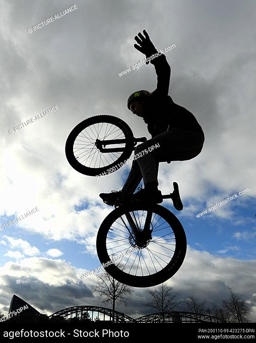 dpatop - 10 January 2020, Hessen, Frankfurt/Main: A teenager jumps with his dirtjump bike on the skater area in the Osthafenpark in front of a cloudy sky