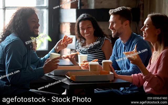 Mixed-race caucasian friends sit at table in cafe eat pizza drink coffee having funny talk. Sharing ordered pizza slices spend Friday in pizzeria yummy fast...