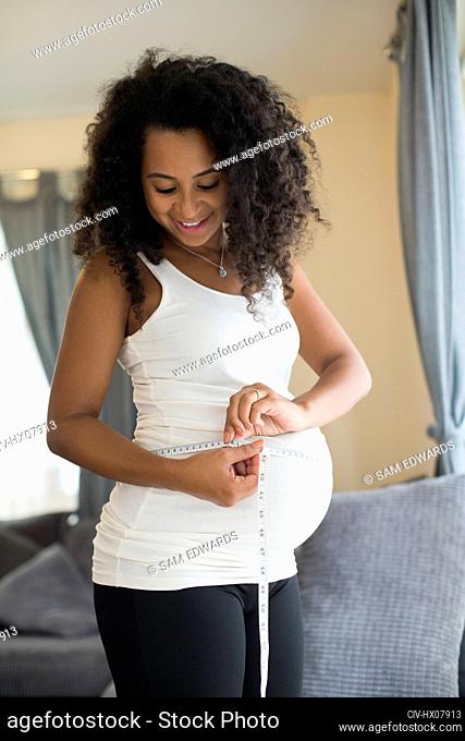 Young pregnant woman measuring stomach with tape measure