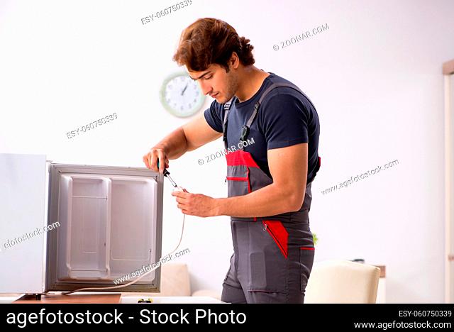 Young handsome contractor repairing fridge
