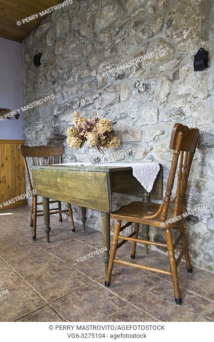 Antique wooden dining table and chairs in entryway with fieldstone wall and terracotta ceramic tile floor inside an old 1820 cottage style fieldstone house