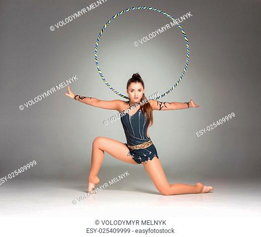 teenager doing gymnastics exercises with colorful hoop on a gray background