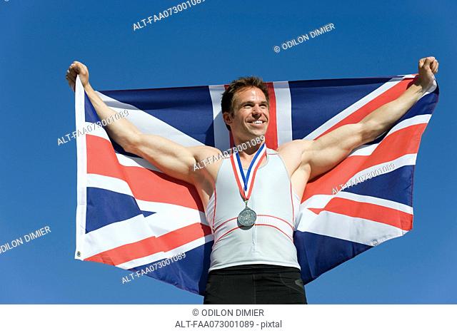 Male athlete on winner's podium, holding up British flag