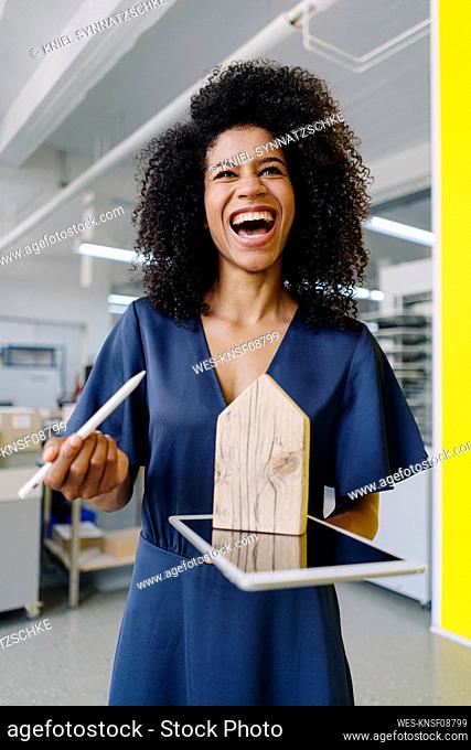 Saleswoman laughing while holding house model on digital tablet at agency