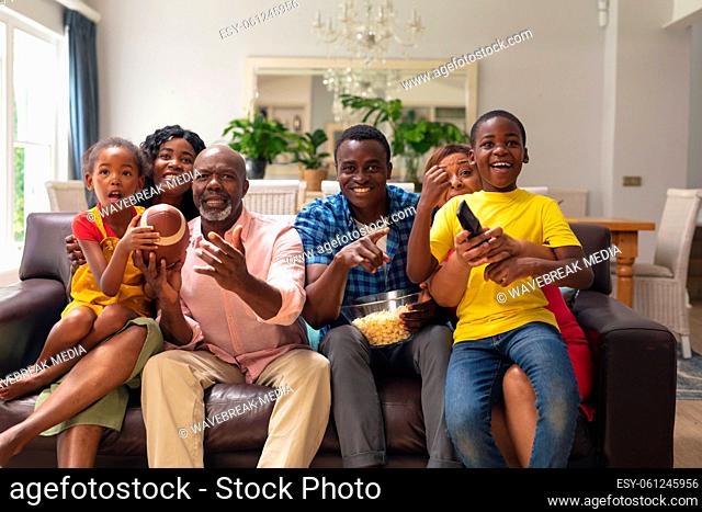 African american multi-generational family cheering while watching rugby match together on tv