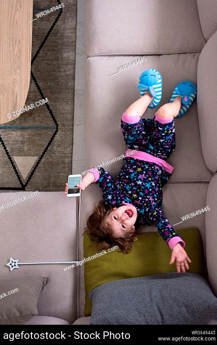 top view of cute little girl using a smartphone and smiling while lying on the sofa at home