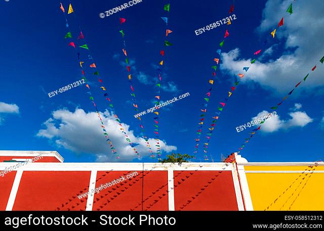 Vibrant flag chains over bright blue sky with white cloudds along colorful colonial building, Valladolid, Yucatan, Mexico