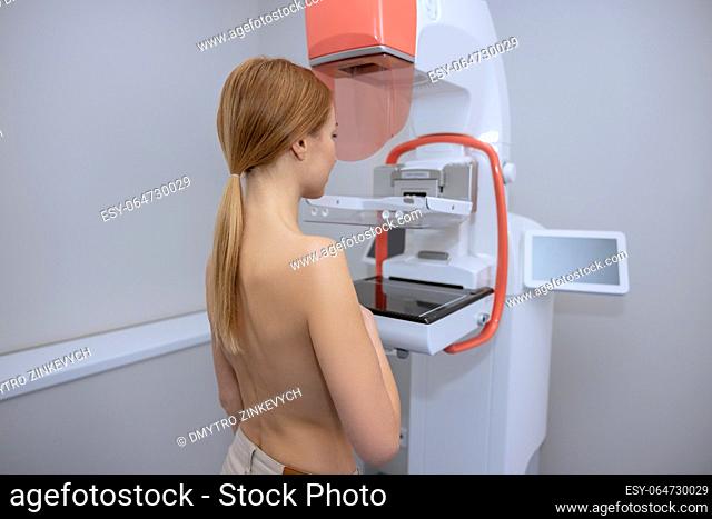 Back view of young woman getting medical test to prevent breast cancer and promoting awareness to get early mammograms in modern clinic