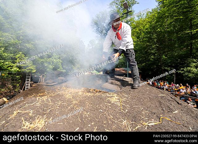 27 May 2023, Saxony, Tharandt: Sven Papperitz stands on the charcoal pile in the Breiten Grund in the Tharandt Forest and throws already pre-charred pieces of...