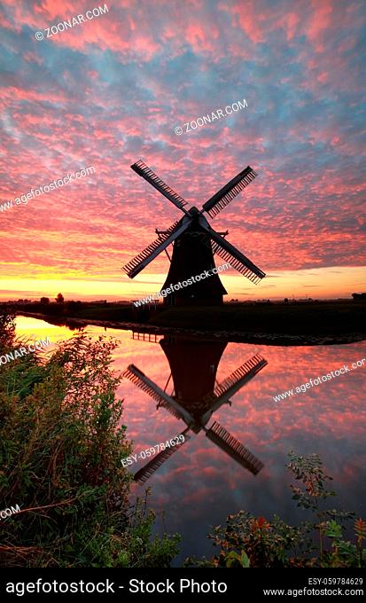 windmill and dramatic sunrise sky reflected in river, Holland