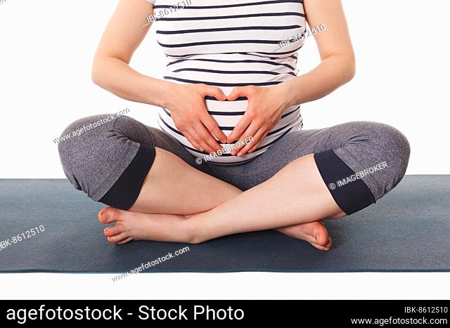 Pregnancy yoga exercise, pregnant woman doing asana Sukhasana easy yoga pose showing heart symbol with her hands isolated on white background