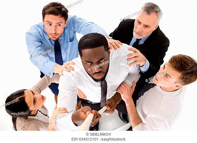 Top view of young African-american businessman reaching up along rope. Other members of business team preventing him from doing it. Isolated on white