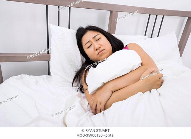 Young woman suffering from stomach ache lying in bed