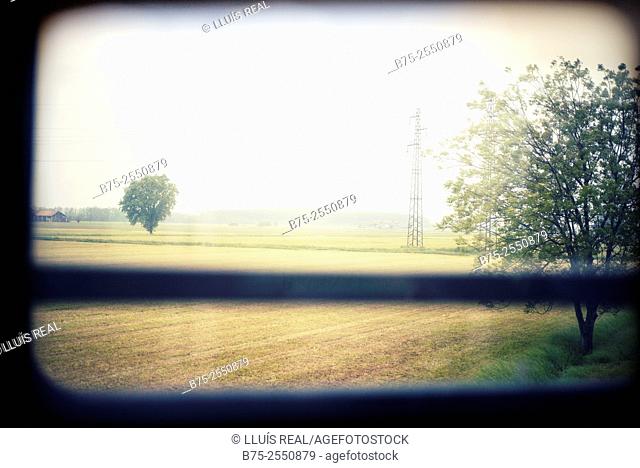 Field landscape with trees and electrical towers seen through the window of a train to Milan. Italy, Europe