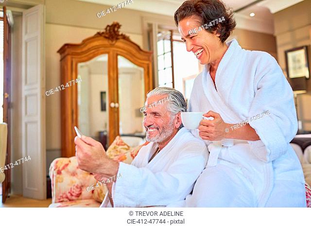 Happy mature couple in spa bathrobes drinking coffee in hotel room