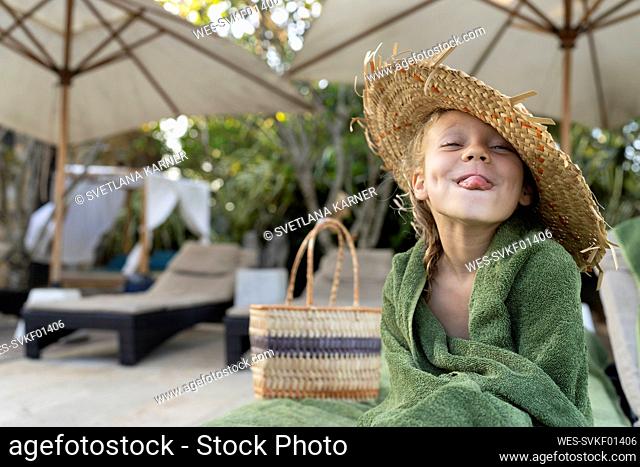Smiling girl wearing straw hat sticking out tongue at beach