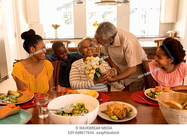 Senior man giving flower bouquet to senior woman while having meal on dining table