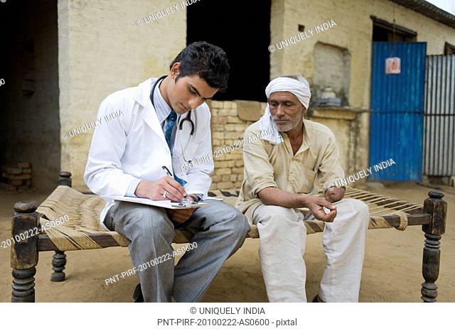 Doctor writing a prescription for a farmer, Hasanpur, Haryana, India