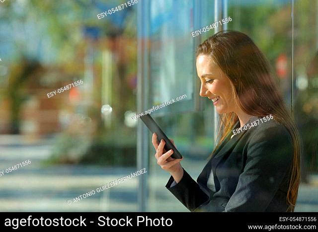 Side view portrait of an executive checking smart phone content waiting in a bus stop