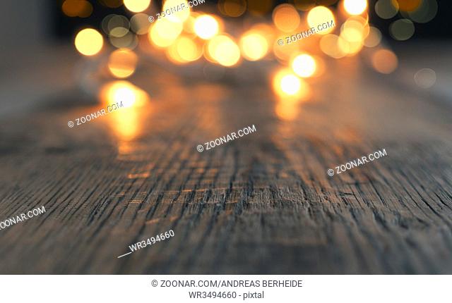 Blurred Christmas lights on a rustic wooden table with space for text or image, selective focus on foreground