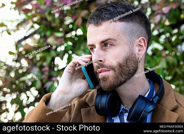 Mid adult businessman wearing headphones talking on mobile phone standing outdoors