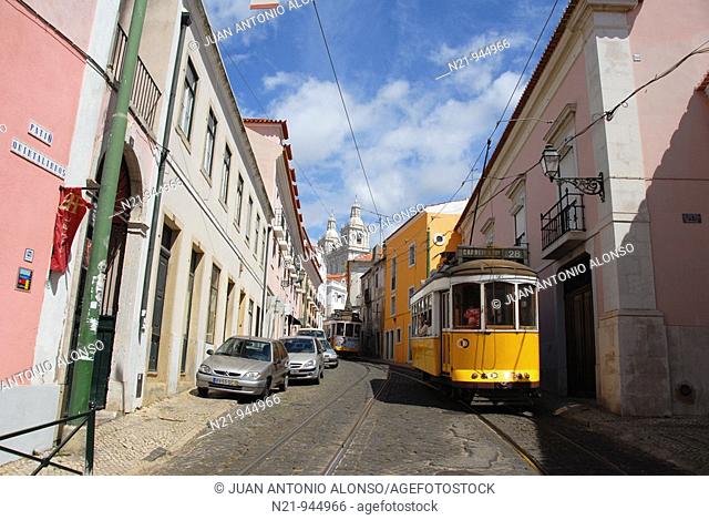 The popular tram 28 through the winding and narrow streets of Alfama. In the background, the towers of  the Mosteriro de Sao Vicente de Fora