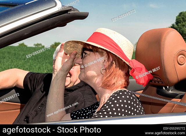Happy older woman with a sun hat and her partner in a luxury convertible car