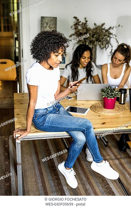 Woman with cell phone sitting on table with friends in background