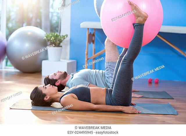 Man and woman holding exercise ball between legs