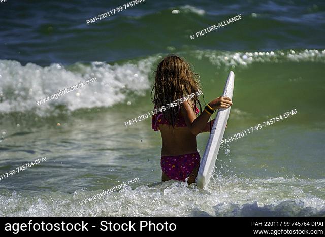 16 January 2022, Brazil, Canasvieiras: A girl goes into the sea with a small board made of Styrofoam. A heat wave is registered in the south of Brazil