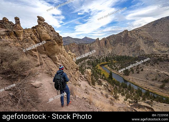 Young man on hiking trail, looking into the distance, view of the course of the Crooked River, canyon with rock formations, Smith Rock State Park, Oregon, USA