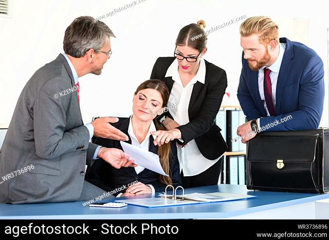 Business team gathers around a desk, discussing a document