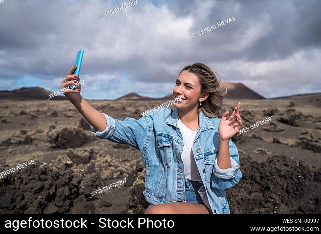 Smiling tourist taking selfie through mobile phone while standing at Volcano El Cuervo, Lanzarote, Spain