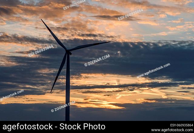 A silhouette of a wind turbine in front of a cloudy sky with sunrise