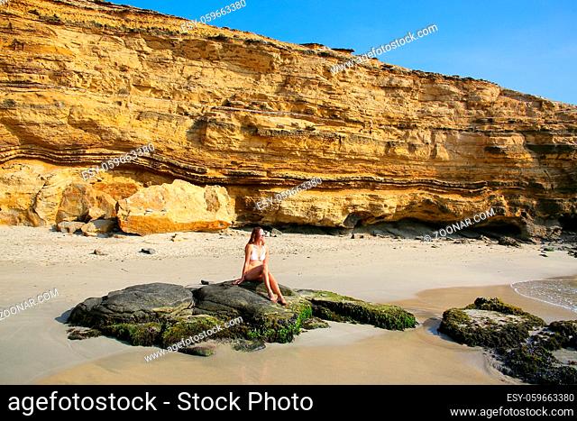 Young woman in bikini sitting at La Mina Beach in Paracas National Reserve, Peru. Main purpose of the Reserve is to protect marine ecosystem and historical...