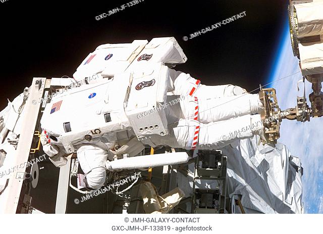 Astronaut Lee M.E. Morin (foreground) works on the International Space Station with his feet secured in a restraint on the end of the station's robotic arm...