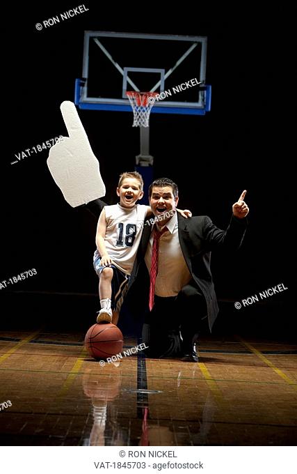 Young boy standing on basketball court with his father looking happy