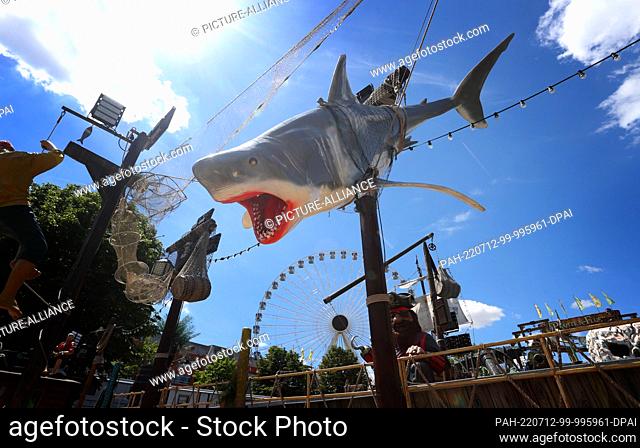 12 July 2022, Bavaria, Würzburg: An imitation shark on a ride stands against a white and blue sky at the Kiliani Folk Festival