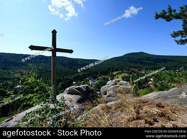 PRODUCTION - 06 July 2023, Saxony, Oybin: View over the summit cross at the fortress and monastery Oybin to the spa of the same name on the border with the...